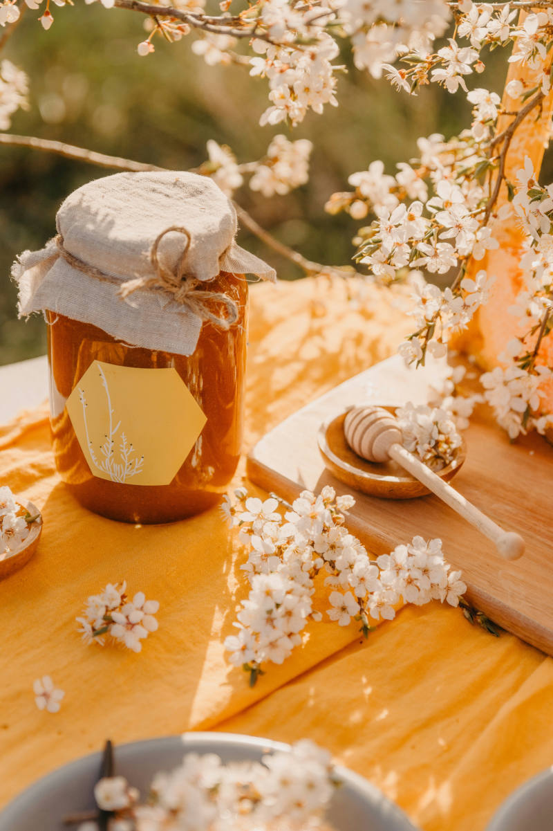 Honigglas mit Blankoetikett auf Tisch mit weißen Blüten