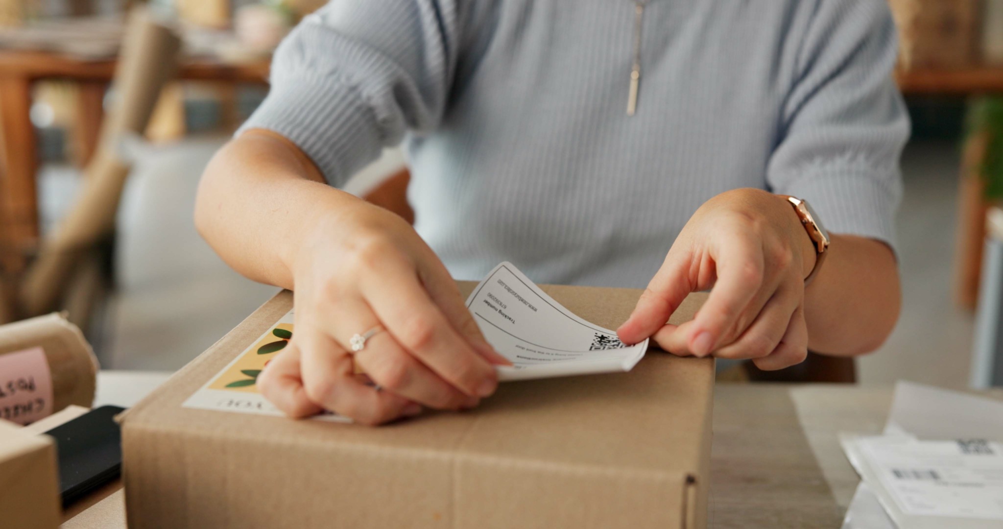 Person klebt mit beiden Händen ein Versandetikett auf ein Paket drauf